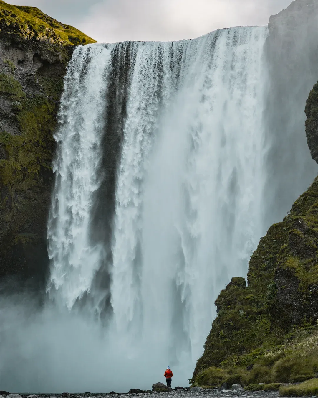 Skógafoss waterfall with a tiny figure at its base.