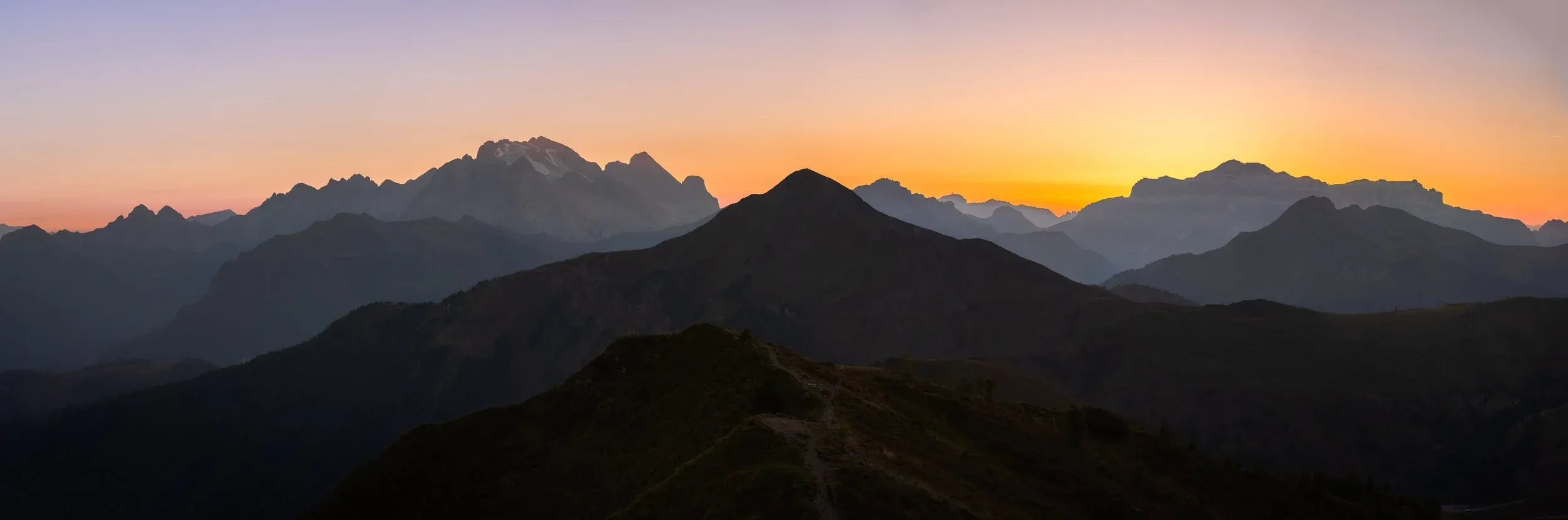 Layered mountain ridges against an orange sunset.